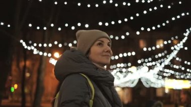 Bir kadın Noel arifesinde akşam sokakta yürür. Noel ve Yeni Yıl 'dan Önce Şenlikli Sokak Işığı.