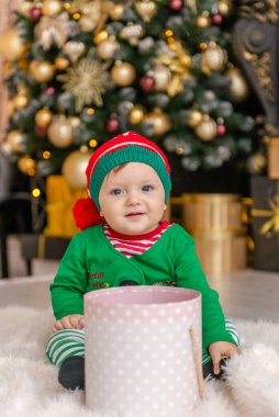 Elf gibi giyinmiş şirin bir çocuk Noel hediyesini süslü bir Noel evinde açıyor..