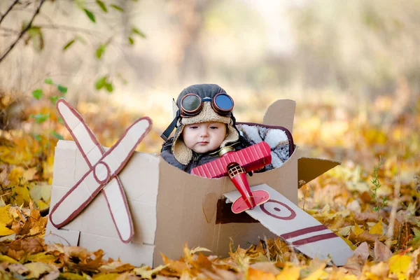 stock image A happy child dreams of traveling in an airplane and plays an airplane pilot. The kid sits in a cardboard plane and pretends to be a pilot in the park in the fall.