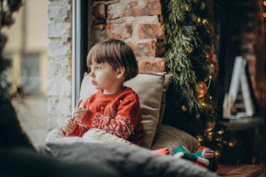 Çocuk pencerede oturur ve Noel Baba 'yı bekler. Noel tatilini bekliyorum. Mutlu bir çocukluk. İtfaiyecileri bekliyoruz..