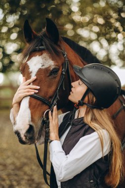 Genç bir dişi binici atının yanında duruyor ve bir yarışa hazırlanıyor. Atlama eğitimini göster. Atları severim..