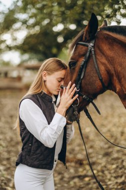 Genç bir dişi binici atının yanında duruyor ve bir yarışa hazırlanıyor. Atlama eğitimini göster. Atları severim..