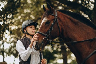 Genç bir dişi binici atının yanında duruyor ve bir yarışa hazırlanıyor. Atlama eğitimini göster. Atları severim..