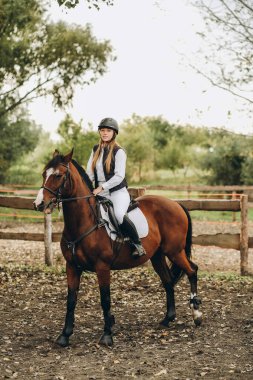 A young female jockey is sitting on her horse in show jumping training. Preparing for the competition. Love for horses.