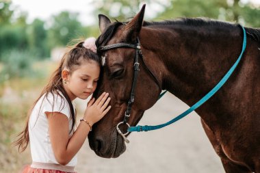 Cute little girl stroking a horse's head on a farm in the countryside in summer. Love for horses.