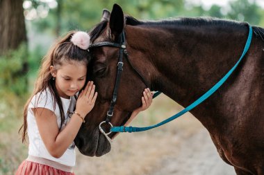 Cute little girl stroking a horse's head on a farm in the countryside in summer. Love for horses.