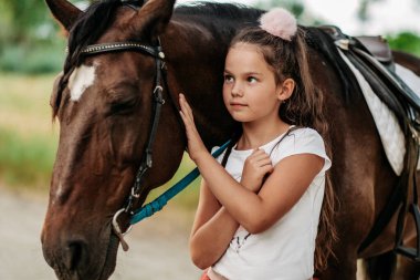 Cute little girl stroking a horse's head on a farm in the countryside in summer. Love for horses.