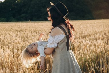 A young beautiful brunette plays with her little child on a walk in a field of sunflowers. Deficit of sunflower oil in the world. Family walk in the countryside in summer on