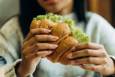 A young African American woman sits in a cafe and eats an appetizing burger. Bad cheap food. Wrong nutrition.