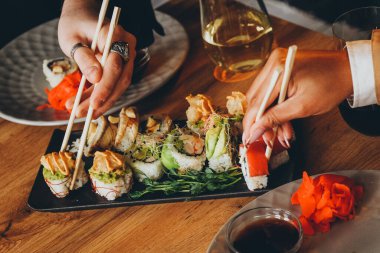 Beyaz bir adam ve siyah bir kadın lezzetli taze suşi yer ve şarap içerler. Bir Japon restoranında öğle yemeği. Asya mutfağı. Eller yakın çekim..