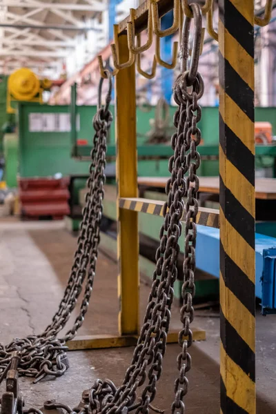 Metal cables and chains for slings hang in the workshop. Sling safety. Regular inspection of slings at the factory.