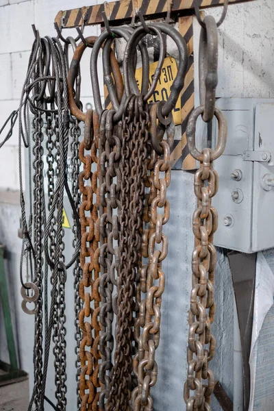 Metal cables and chains for slings hang in the workshop. Sling safety. Regular inspection of slings at the factory.
