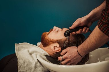 A professional barber cuts his beard to a young hipster man. Beard trim at the barbershop. Stylish beard cut.