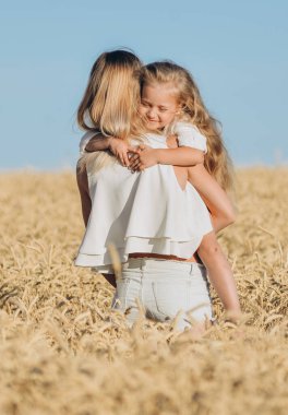 Buğday yetiştiriyorum. Gıda güvenliği. Bir kadın küçük kızını kollarına alır ve yazın bir buğday tarlasında durur..