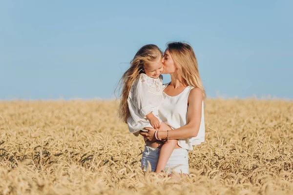 Growing wheat. Food security. A woman holds her little daughter in her arms and stands in a wheat field in summer.