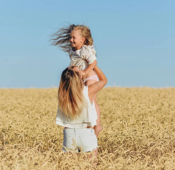 Growing wheat. Food security. A woman holds her little daughter in her arms and stands in a wheat field in summer.