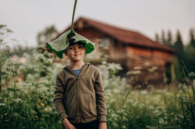 Çocuk elinde büyük bir dulavrat yaprağı tutuyor. Çocuk büyük bir çarşafla oynuyor. Bir dağ köyünde akşam yürüyüşü. Yazın dağlara turist gezisi.