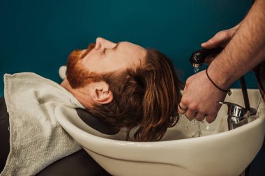 A professional barber cuts his beard to a young hipster man. Beard trim at the barbershop. Stylish beard cut.
