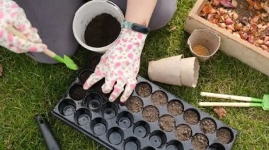 Bir kadın baharda hücrelere tohum ekmek için toprağı hazırlıyor. Yakından çekilen eller dünyayla birlikte hareket ediyor. Baharda bir serada çiçek ve sebze yetiştirmek..