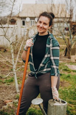 Bir çiftçi kadın baharda elinde tarımsal aletlerle bir sebze bahçesinde duruyor. Bir kadın bahçede bahar işi yapıyor..