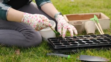 Bir kadın baharda hücrelere tohum ekmek için toprağı hazırlıyor. Yakından çekilen eller dünyayla birlikte hareket ediyor. Baharda bir serada çiçek ve sebze yetiştirmek..