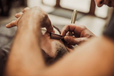 A professional barber cuts his beard to a young hipster man. Beard trim at the barbershop. Stylish beard cut.