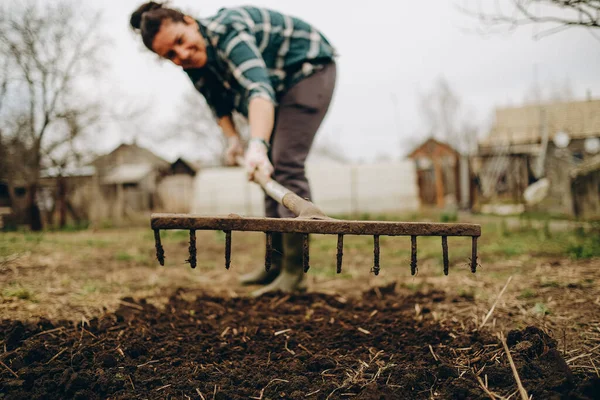 Stock image Young woman farmer works with a rake in a field in spring. Preparing the soil before planting. Close-up of a rake in the hands of a woman.