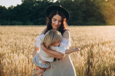 A young beautiful brunette plays with her little child on a walk in a field of sunflowers. Deficit of sunflower oil in the world. Family walk in the countryside in summer on