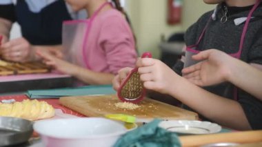 Çocuk yemek hazırlıyor. Çocuklar için yüksek lisans sınıfı. Çocuk peynirli bir yemek hazırlamak için rendelenmiş peyniri rendeliyor..