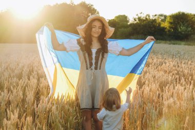 Yazın Ukrayna bayrağıyla buğday tarlasında bebekle yürüyen genç bir kadın. Ukrayna 'nın Rusya' ya karşı savaştaki zaferi. Ukrayna kazanacak..