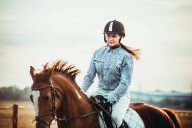 Genç bayan sporcu ata biniyor. Baharda sahada atlama eğitimi. At biniciliği. Sporda cinsiyet eşitliği.