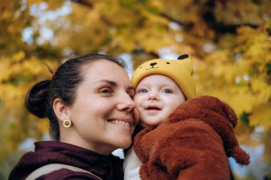 A woman walks in the park in autumn with her child. A young woman holds her baby in her arms and stands under a tree. Family walks in autumn in the park.