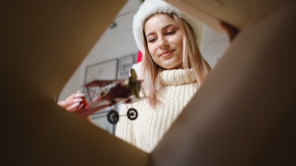 クリスマスイブに子供たちのための箱にクリスマスプレゼントを飾る女性 サンタの帽子の美しい金髪のママは贈り物を準備する — ストック動画