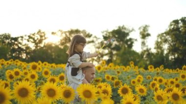 Bir baba, yaz ayçiçeği tarlasında Down sendromlu kızını omuzlarında taşır..