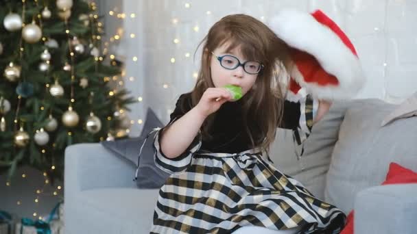 ダウン症の少女が部屋のソファーに座り クリスマスイブで笑いを食べる — ストック動画