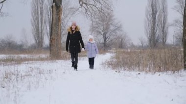 Anne ve kızı kışın parkta yürürler. Noel için aile kışı yürüyüşleri. Çocukların düzgün yetiştirilmesi.
