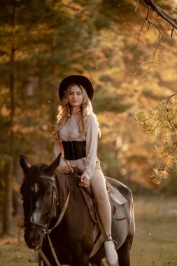 Genç ve güzel bir kadın sonbaharda ormanda ata biner. Sonbaharda akşamları ata binmek. At yarışı sporu için çiftlikte at yetiştiriyorum..