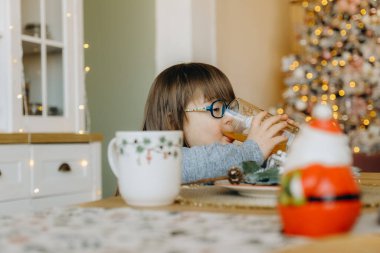 Down sendromlu bir kız portakal suyu içer ve Noel arifesinde masada oturur..