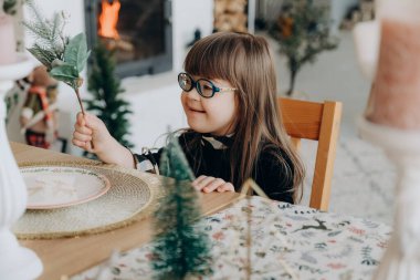 Down sendromlu bir kız Noel arifesinde şenlikli bir Noel masasında oturuyor. Down sendromlu bir çocuk yetiştirmek.
