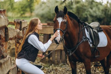Genç bir dişi binici atının yanında duruyor ve bir yarışa hazırlanıyor. Atlama eğitimini göster. Atları severim..