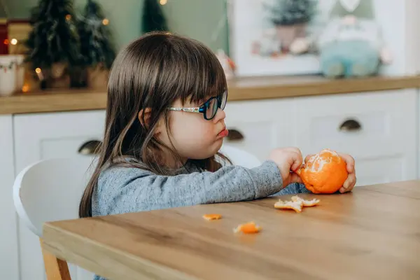 Raising a child with Down syndrome. A girl with Down syndrome peels an orange and sits at the dinner table on Christmas Eve.