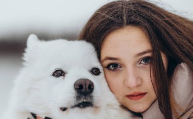 Kışın sevgili evcil hayvanı Samoyed ile parkta bir gölün kıyısında yürüyen bir kız. Kışın köpeği gezdiriyorum..