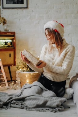 Noel Baba şapkalı genç ve güzel bir kadın elinde bir Noel hediyesi tutuyor. Noel 'i evde kutluyoruz.