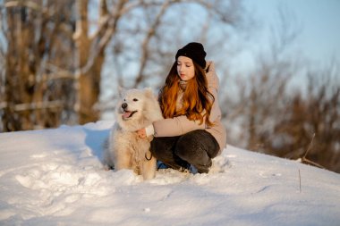 Kışın sevgili evcil hayvanı Samoyed ile parkta bir gölün kıyısında yürüyen bir kız. Kışın köpeği gezdiriyorum..