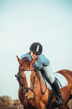 Genç bayan sporcu ata biniyor. Baharda sahada atlama eğitimi. At biniciliği. Sporda cinsiyet eşitliği.