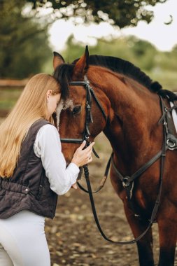 Genç bir dişi binici atının yanında duruyor ve bir yarışa hazırlanıyor. Atlama eğitimini göster. Atları severim..