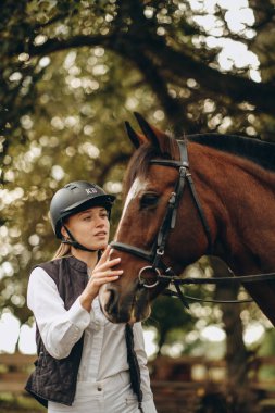 Genç bir dişi binici atının yanında duruyor ve bir yarışa hazırlanıyor. Atlama eğitimini göster. Atları severim..
