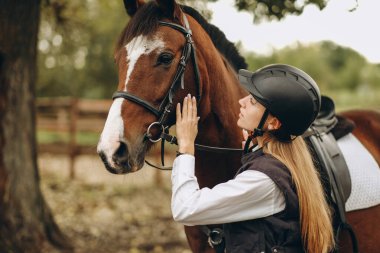 Genç bir dişi binici atının yanında duruyor ve bir yarışa hazırlanıyor. Atlama eğitimini göster. Atları severim..