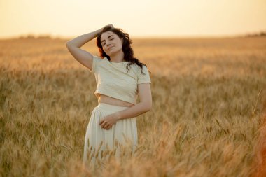 Genç bir esmer yazın günbatımında buğday tarlalarında yürür. Organik buğday ve arpa yetiştiriyor..