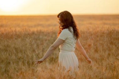 Genç bir esmer yazın günbatımında buğday tarlalarında yürür. Organik buğday ve arpa yetiştiriyor..
